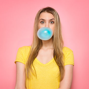 Cute girl blowing blue bubble gum near pink wall