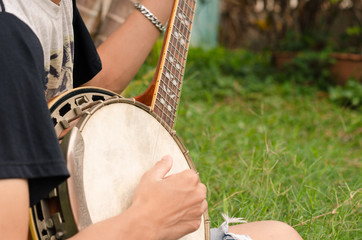 Young man sitting banjo on the lawn happily.