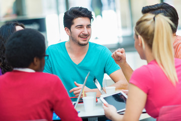 A group of teenagers sitting at the table in cafe, using laptop and drinking orange juice.