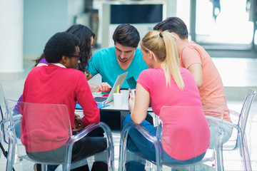 Obraz premium A group of teenagers sitting at the table in cafe, using laptop and drinking orange juice.