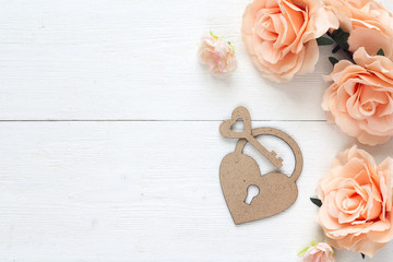 Background with decorative padlock-heart, key and lovely roses on a white wooden table. Place for the text.