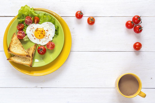 Healthy Breakfast with heart-shaped fried egg, toast, cherry tomato, lettuce on colored plates and coffee. Top view.