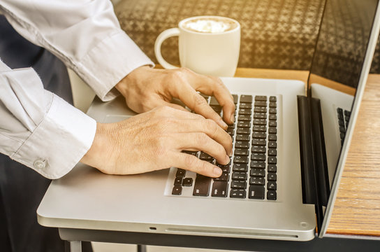 Close up of a man hands typing in a laptop in a coffee shop