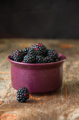 Fresh blackberries in a purple ceramic bowl on a wooden background. Close up vertical and copy space.