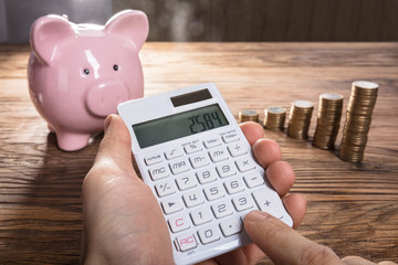 Person Calculating On Calculator With Piggybank And Coin Stacked