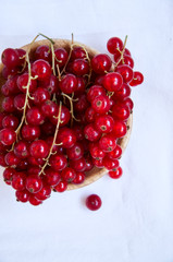 Heap of fresh ripe raw red currants in a small wooden plate on a white napkins. Rustic style and copy space wooden background.