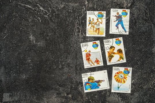 set of randomly lying postage stamps printed in Cuba shows athletes and various sports, devoted to 4 Spartakiad,  series, circa 1977, on a dark black cement background