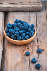 Heap of fresh ripe raw bluberries in a small wooden plate on a wooden background. Rustic style and copy space.