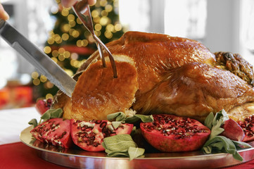 Carving garnished roasted turkey on Christmas decorated table with Christmas tree blurred in the background