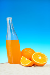 The bottle of orange juice and fruits on the beach