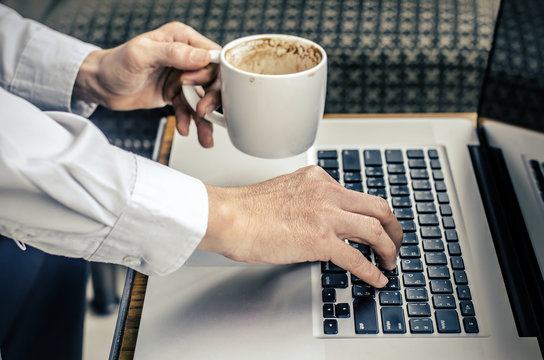 man with a cup of coffee working on his laptop