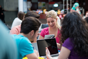 A group of teenagers sitting at the table in cafe, using laptop and drinking orange juice.