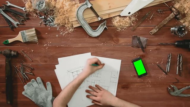 Top view craftsman hands drawing floor plan and iphone with green screen lying on the table