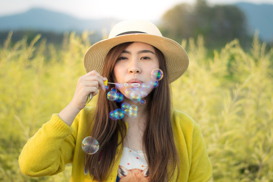 Asian woman is enjoy blow bubble at flower field during summer time.