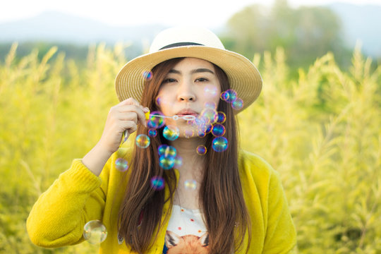 Asian woman is enjoy blow bubble at flower field during summer time.