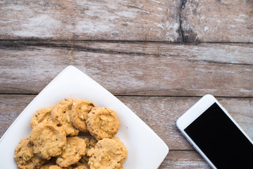 Cookies in dish and phone on wooden table background