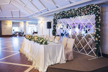 Long dinner table decorated with white flowers stands before the mirror