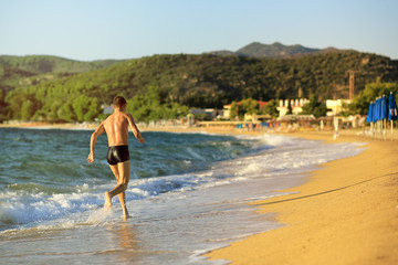 Fototapeta premium A young guy runs along an empty beach at sunset. Greece, Chalkidiki, Sithonia