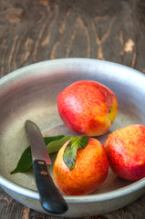 Close up of fresh ripe honeyed nectarines (peaches)  with leaves and water drops in a vintage bowl on a wooden board. Summer fruits concept. Rustic style.