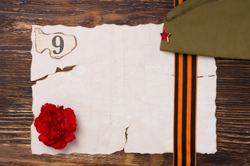 Burning sheet of paper on the table, with a red carnation and number 9, and a cap with a red star, the background to the day of victory