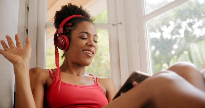 Black girl lying on couch and singing song, young african american woman relaxing. Happy latina sitting on sofa and listening to music. Hispanic people and lifestyle. Leisure and relaxation at home
