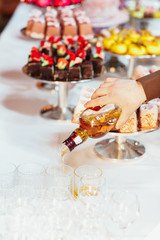 Man pours drink in glasses on table with sweets