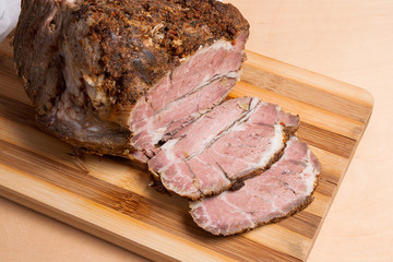Sliced baked pork with herbs and spice on wooden board.