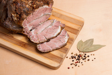 Sliced baked pork with herbs and spice on wooden board.