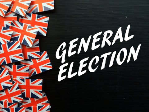The words General Election in white text on a blackboard with several Union Jack flags of the United Kingdom
