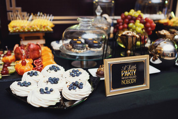 Black plate with blueberries on cakes stands before lettering 'A little party never killed nobody'