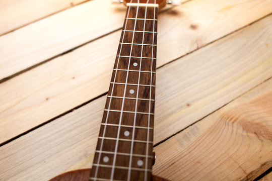 Hawaiian four-stringed guitar ukulele close-up frets on wooden background