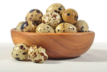 Quail eggs in a wooden bowl on a white