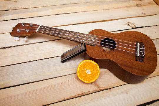 Hawaiian four-stringed ukulele guitar with sliced juicy orange oranges and an iron lip accordion on wooden background