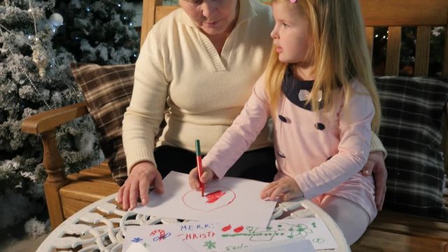 Woman and Her Granddaughter Drawing Together Kid's Colorful Drawings on a Table New Year Interior and Lights Are Traditional Christmas Eve at Home