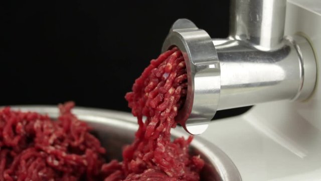 Meat grinder closeup. Grinding meat with mincing machine over black background