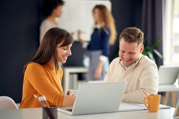 Young happy people discussing business sitting at the desk with laptop in modern light office 