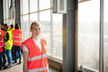 Obraz premium blonde woman in overalls, on the tour of the brewery plant in industrial premises, amid crowds of people in vests, inspecting a factory for training purposes