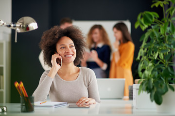 Young happy people discussing business standing at the whiteboard in modern light office, beautiful woman sitting at the table at forefront