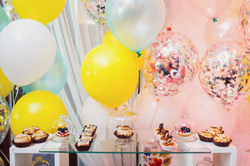 Colorful balloons hang behind glass box with cakes