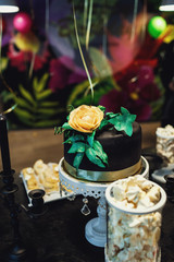 Little black cake decorated with green leaves and beige rose