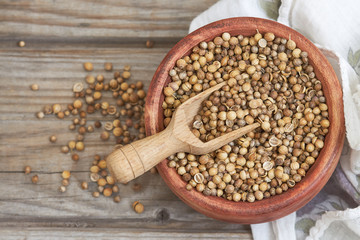 Dried coriander seeds and scoop in wooden bowl on grey rustic background. Top view with copy space