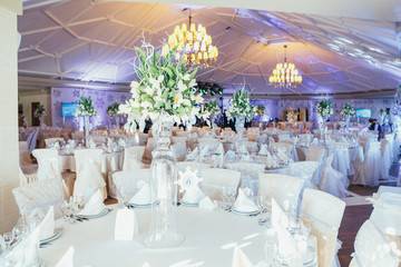 Round dinner tables covered with white clothes stand in bright restaurant hall