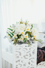 Bouquet of white flowers and green leaves stands on white chest