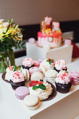 Tasty macaroons and cupcakes on white dinner table