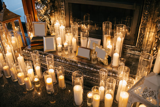 Shiny candles in glass vase stand before the fireplace