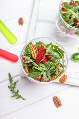 Fresh salad with strawberries, arugula and pecans on a white wooden background. Concept of Healthy Food. Top view