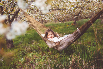 Child girl is resting in hammock in cherry garden