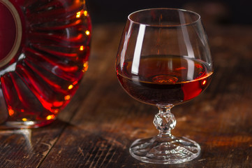 Glass of cognac and  bottle of cognac on vintage wooden background. Low depth of field.