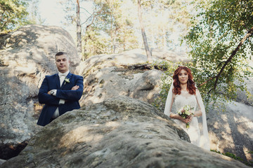 Bride and groom stand apart on the rocks in the forest