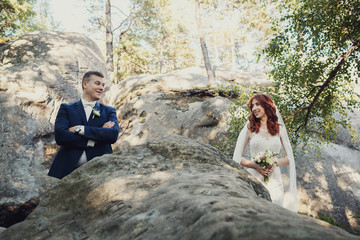Bride and groom stand apart on the rocks in the forest
